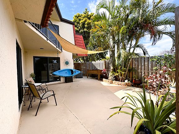 Large patio with lush palms, sunshade, and planter is perfect for entertaining, grilling, or gardening.