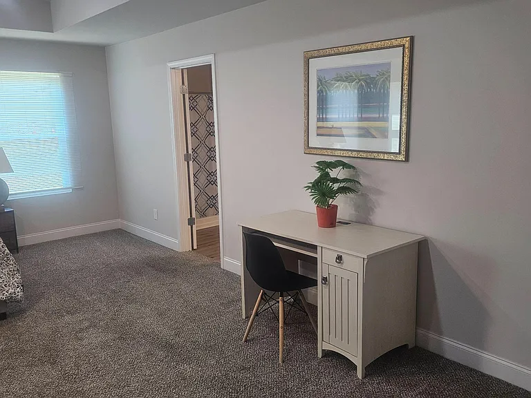 Carpeted bedroom with a window for natural light, furnished with a bed and a dedicated desk/work area near the ensuite.