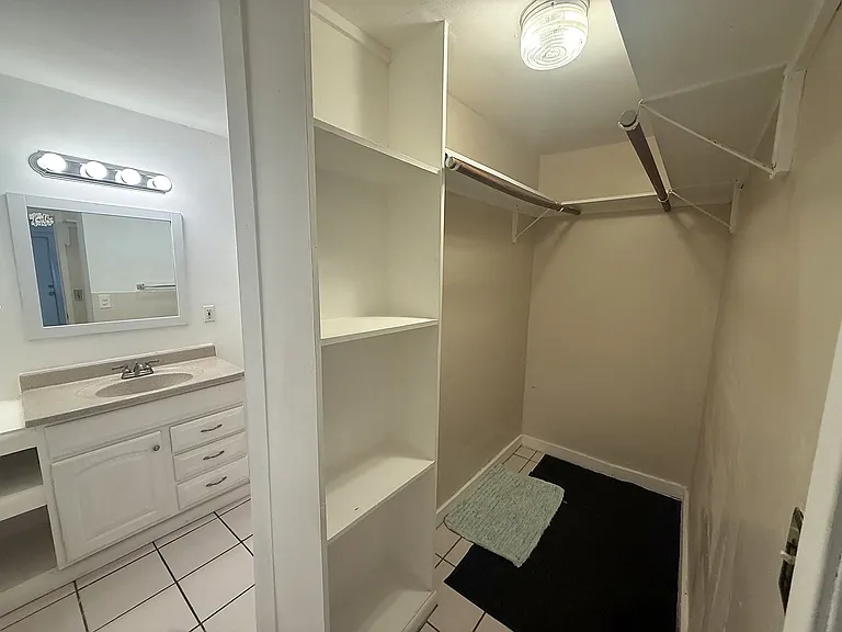Walk-in closet and dressing/storage area with built-in shelving and multiple hanging rods, conveniently located adjacent to the bathroom.