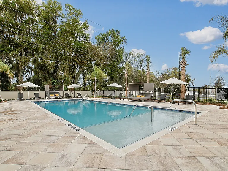 Inviting outdoor swimming pool area with chic lounge chairs and umbrellas set against a backdrop of lush greenery and blue skies.