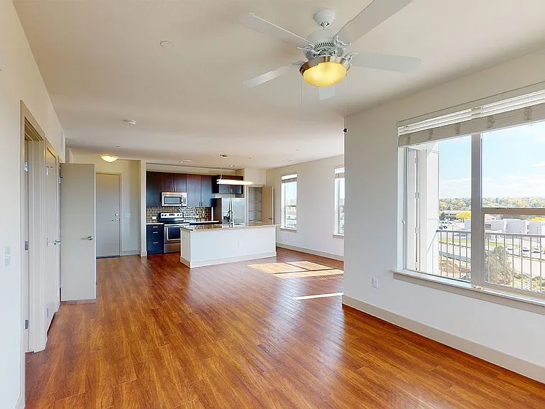 Apartment kitchen with stainless steel appliances, dining and living room with wood-style flooring.