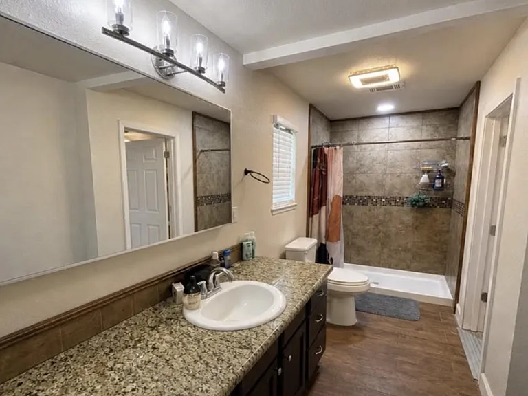 Spacious bathroom with granite vanity, large mirror, and a tiled walk-in shower plus additional storage.