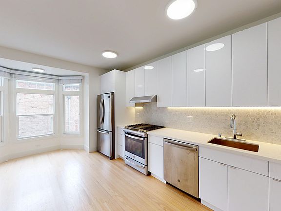 Modern kitchen featuring stainless steel appliances, cabinetry, and a hexagonal backsplash, illuminated by warm under-cabinet lighting.