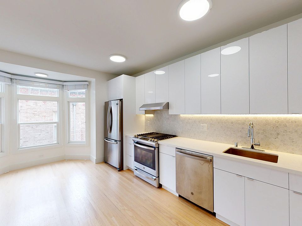 Modern kitchen featuring stainless steel appliances, cabinetry, and a hexagonal backsplash, illuminated by warm under-cabinet lighting.