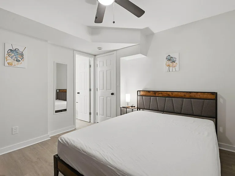Furnished bedroom with wood-style flooring, ceiling fan, bedside table, and full-length mirror for easy daily routines.