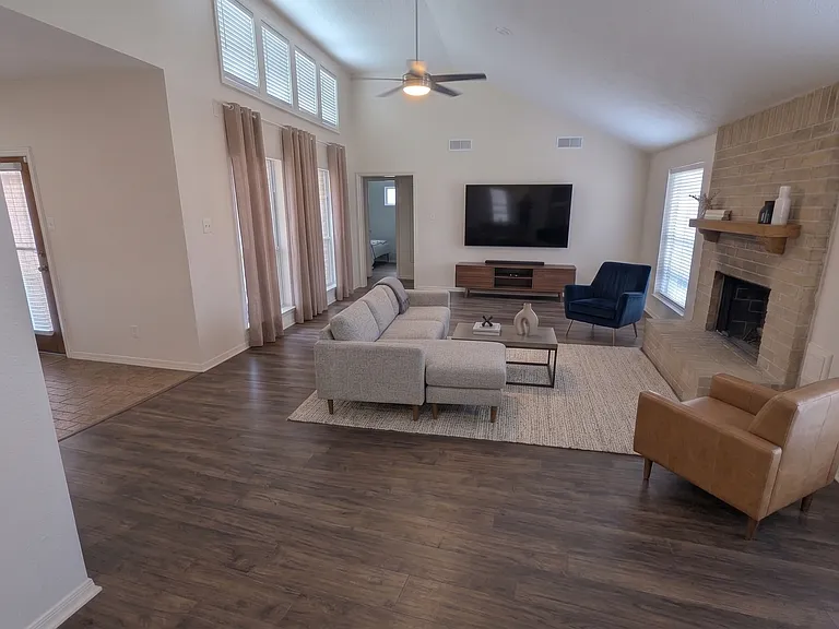 An AI representation of the spacious living room with furnishings. The natural light plays well with the brand new luxury vinyl plank floors for a clean but warm, comfortable look. The gas-log fireplace adds charm.