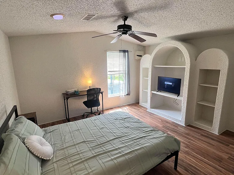 Furnished bedroom with ceiling fan, window for natural light, work desk, and built-in shelving with TV niche.