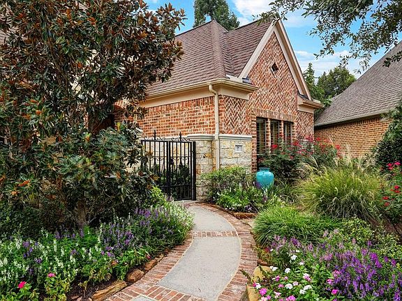 Lush gardens follow the brick banded-walk to the gated stone and brick courtyard entry.