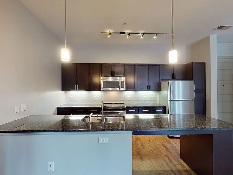 Apartment kitchen with stainless steel appliances, wood-style flooring, and granite countertop peninsula (shown here). Kitchen island available in select homes.