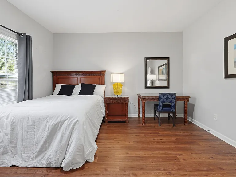 Hardwood floors, window with blinds and black out curtains, and a dedicated desk area for work or study.