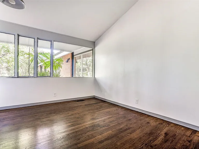 Vaulted ceiling room featuring a multi-pane window with exterior foliage, dark wood-finish flooring, and white painted walls
