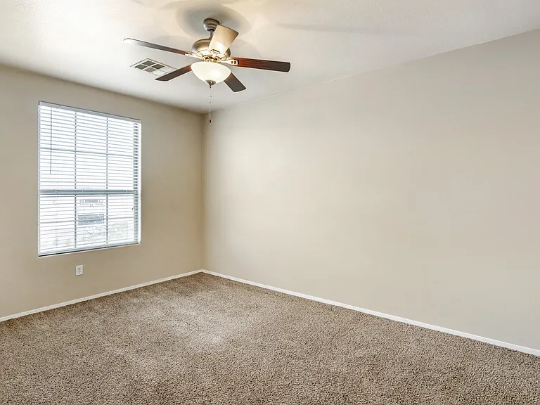 Generously sized bedroom adorned with plush carpeting and equipped with a soothing ceiling fan to enhance your comfort