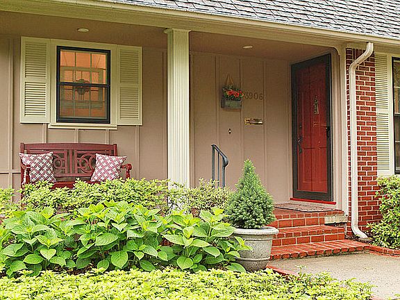 Guests enter the home from the covered front porch framed by thriving landscape plantings.