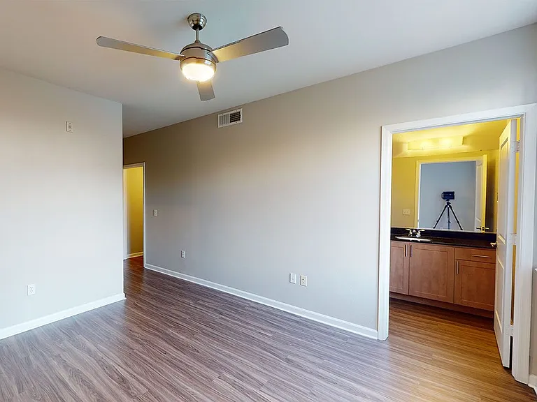 Spacious apartment bedroom with attached bathroom and wood-style flooring.