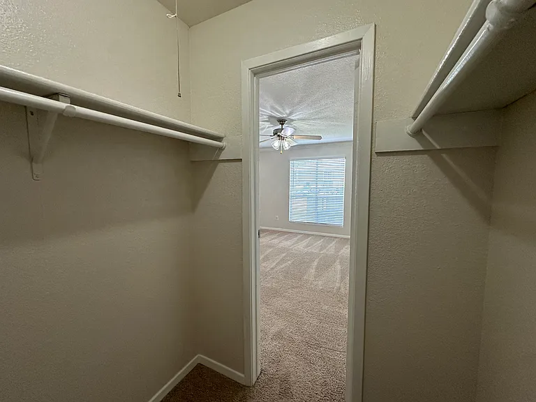 Bright walk-in closet leading to a carpeted bedroom with ceiling fan and natural light. Bright walk-in closet leading to a carpeted bedroom with ceiling fan and natural light.