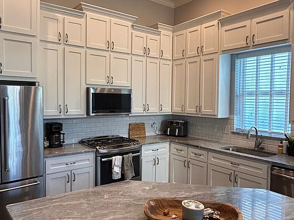 The kitchen has high, molded cabinetry, ample counterspace and lighting, an island, and all standard appliances