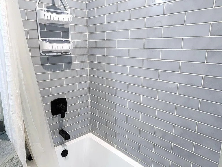 Tiled tub/shower combo with a rain-style showerhead, matte black fixtures, and built-in shelving for bath essentials.
