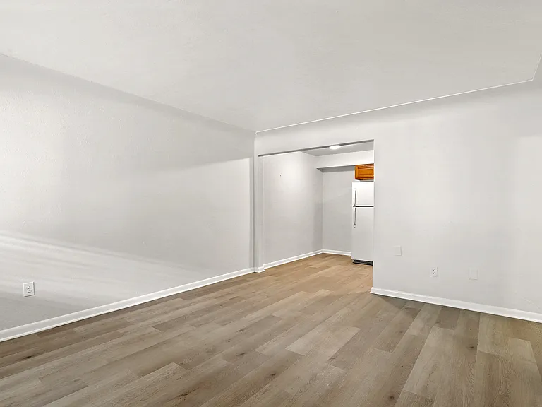Bright and spacious open-plan living area with sleek laminate wood flooring and crisp white walls, leading to a cozy kitchen nook with modern appliances.
