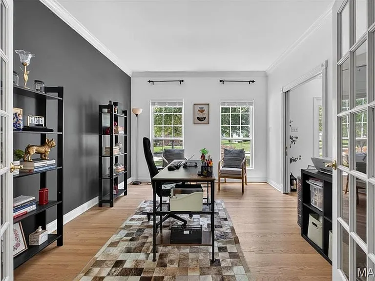 French doors opening to a versatile interior space featuring wood-finish flooring, a contrasting accent wall, and crown molding