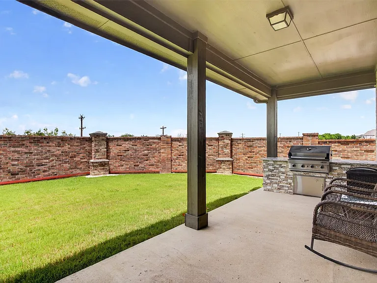 Covered patio featuring an outdoor kitchen with built-in grill, stone facade, and concrete flooring