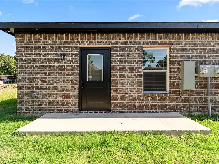 Brick exterior featuring a black door with a clear glass insert, an exterior light fixture, and a window with blinds