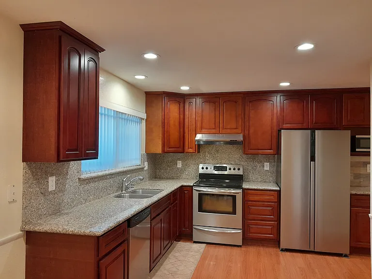 Renovated kitchen with granite countertop, stainless steel appliances, recessed LED lights, laminate wood floor, and a walk-in pantry