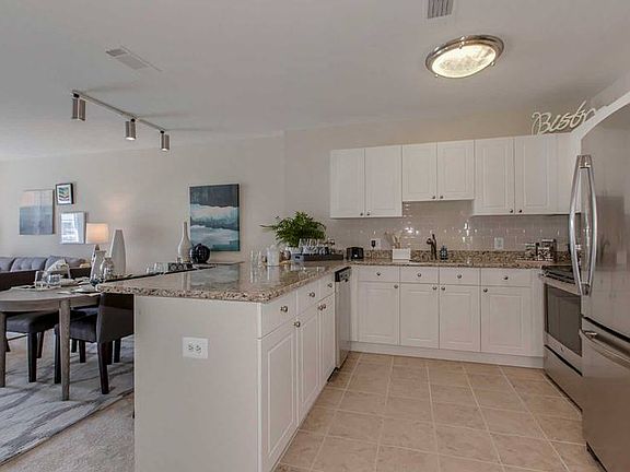 Living and dining areas and open concept kitchen with white cabinetry, cream tile backsplash, stainless-steel appliances, granite countertops and hard surface flooring