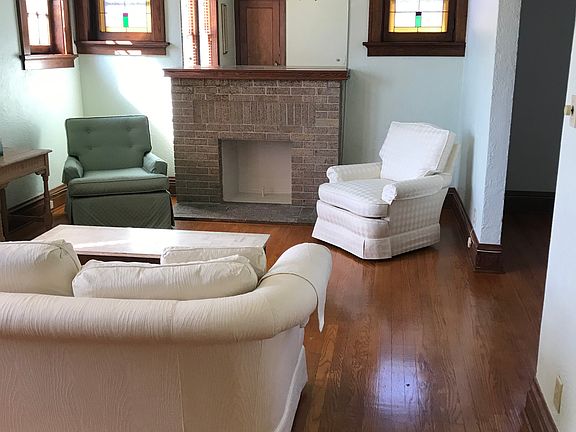 Living room, no furniture available. Ornamental fireplace, stained glass windows, ceiling fan. Wood Blinds. Southern exposure.