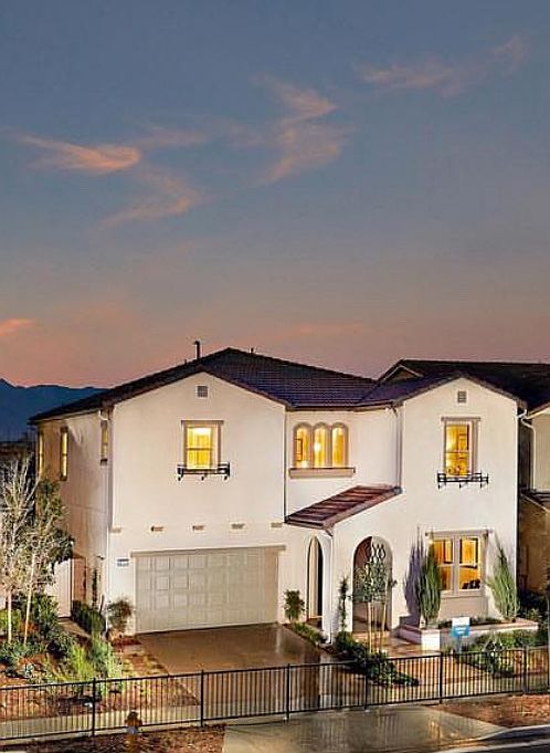 Two-story, Mediteranean-style house at dusk. With car garage with a large, beige door. Arched entryways, including a prominent archway over the front door.
Decorative, wrought-iron railings on the small balconies and window boxes.