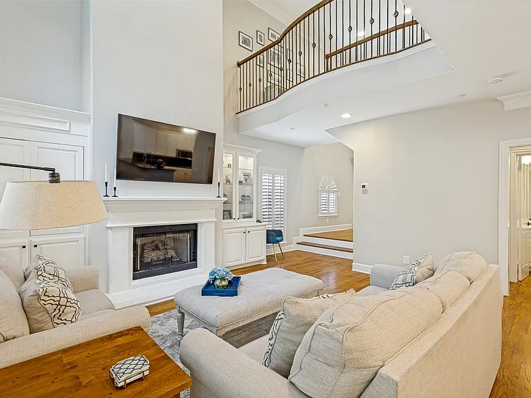 Two-story living area featuring a fireplace with a white mantel, built-in cabinetry, wood-finish flooring, and a curved second-story balcony with iron railings