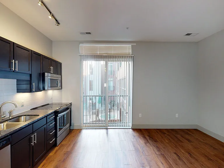 Apartment kitchen with stainless steel appliances, dining and living room with wood-style flooring and balcony or patio in select homes.
