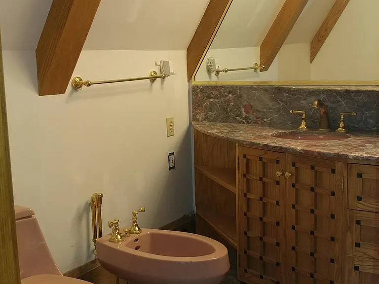 Master bathroom with double-sink vanity, marble countertop, and custom lattice cabinetry under a vaulted ceiling with exposed beams.