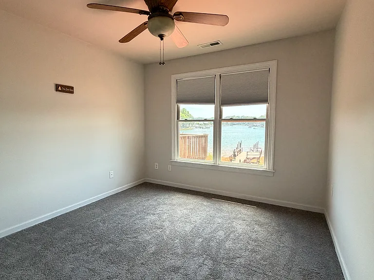 Cozy water-view bedroom with a large front window framing the lake, a ceiling fan for year-round comfort, and a dedicated closet for storage.