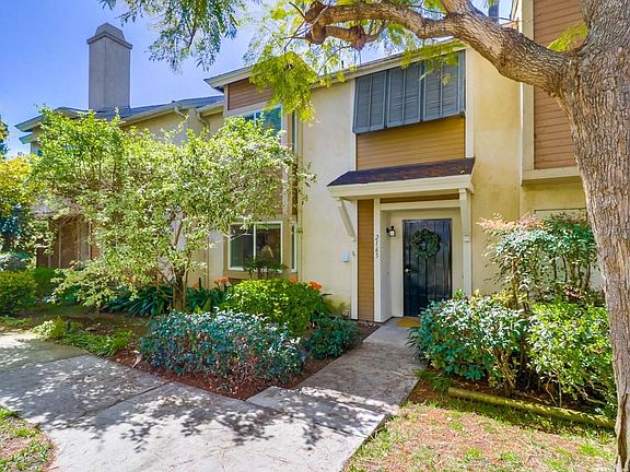 Quiet front entrance surrounded by trees, bushes, grass and flowers.