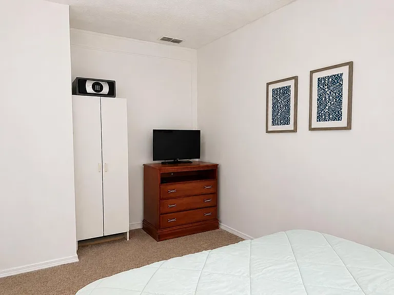 Furnished bedroom with wardrobe storage, dresser with TV, and carpeted flooring for comfortable everyday living.