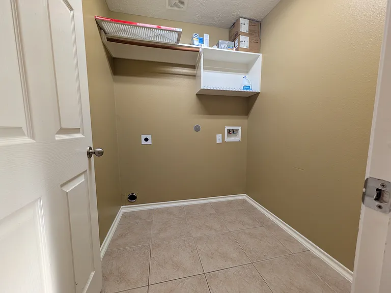 Conveniently located laundry room with durable tile flooring, washer and dryer hookups, and a built-in upper shelf for storage.
