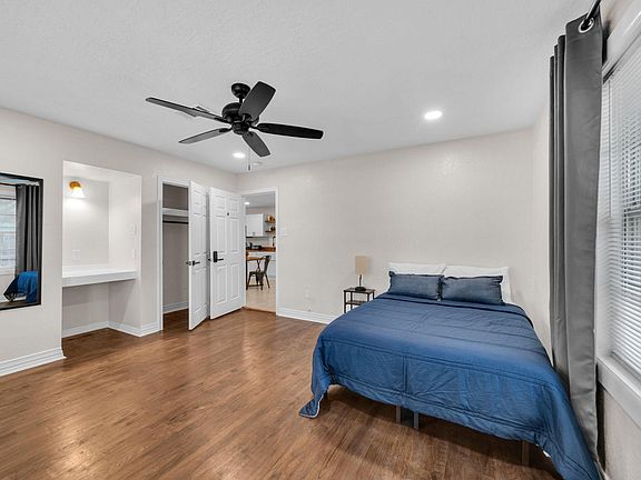 Spacious bedroom with hardwood floors, ceiling fan, and large window with blinds, plus a built-in desk nook.