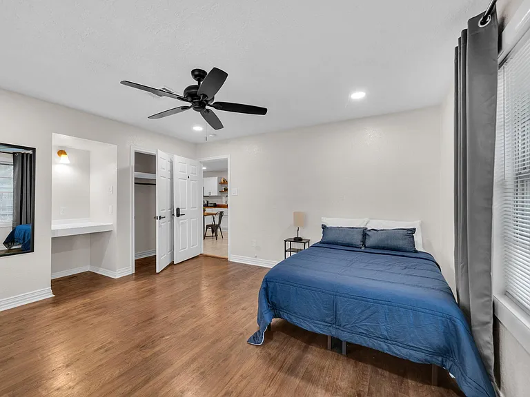 Spacious bedroom with hardwood floors, ceiling fan, and large window with blinds, plus a built-in desk nook.