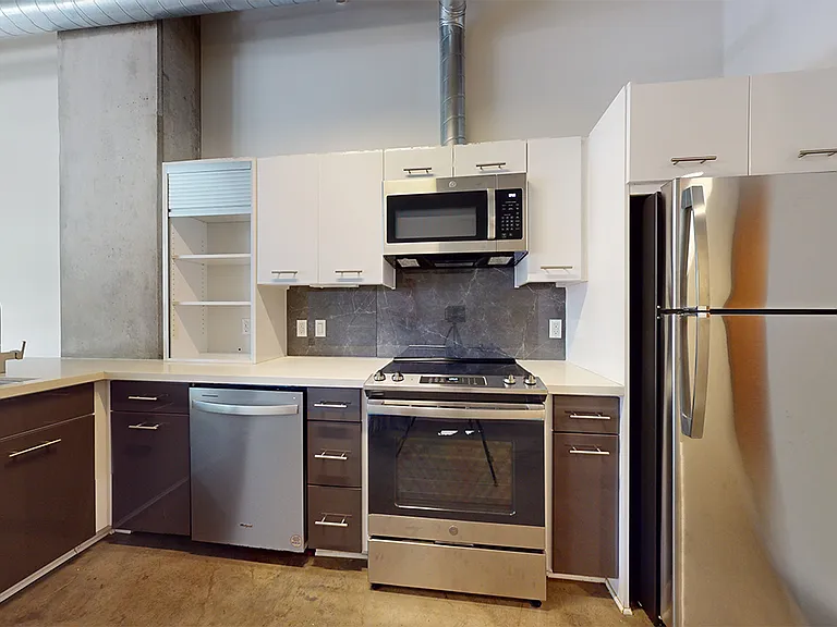Apartment kitchen with stainless steel appliances, quartz countertops and concrete flooring.