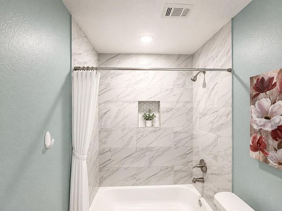 Updated tub/shower combo with marble-look tile surround, built-in niche shelving, and contemporary brushed hardware.