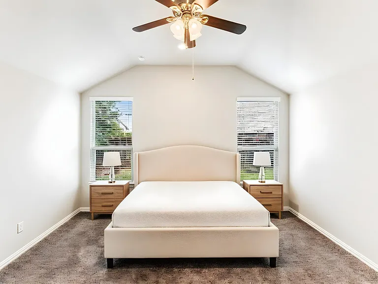 Vaulted ceiling bedroom featuring two windows with horizontal blinds, a ceiling fan with light fixture, and brown carpet flooring
