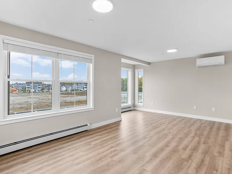 Bright living room with LVP flooring, large windows, and modern climate control.