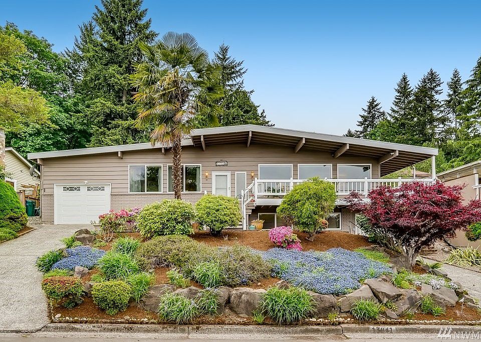 Welcome Home!! Palm tree, mature landscaping, wrap around covered deck to enjoy the view, driveways with 2 garages on either side of the home and a quiet neighborhood