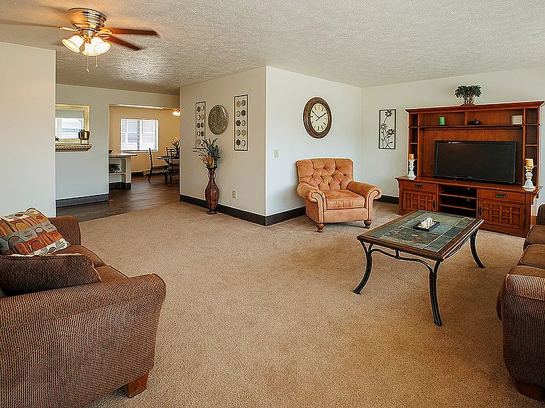 Warm and inviting living room with plush seating, elegant ceiling fan, and stylish decor opening into a well-lit dining area.