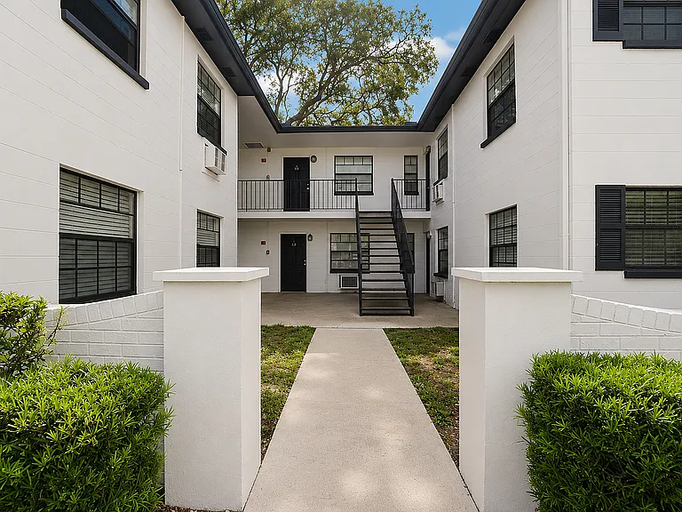 Charming courtyard entrance of a modern apartment complex, featuring sleek black accents and lush greenery.