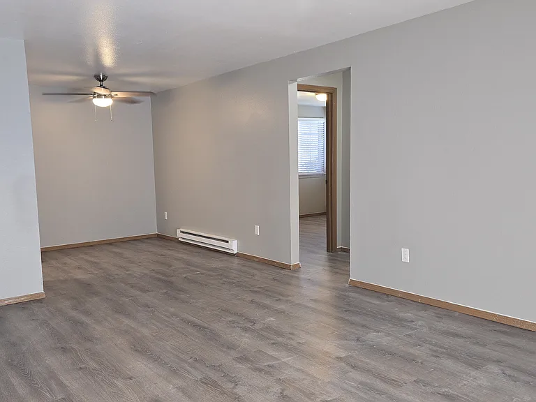 Bright, spacious living room with open flow to dining area and hallway. Features wood-style flooring, neutral finishes, and a ceiling fan_perfect for comfortable living and easy entertaining.