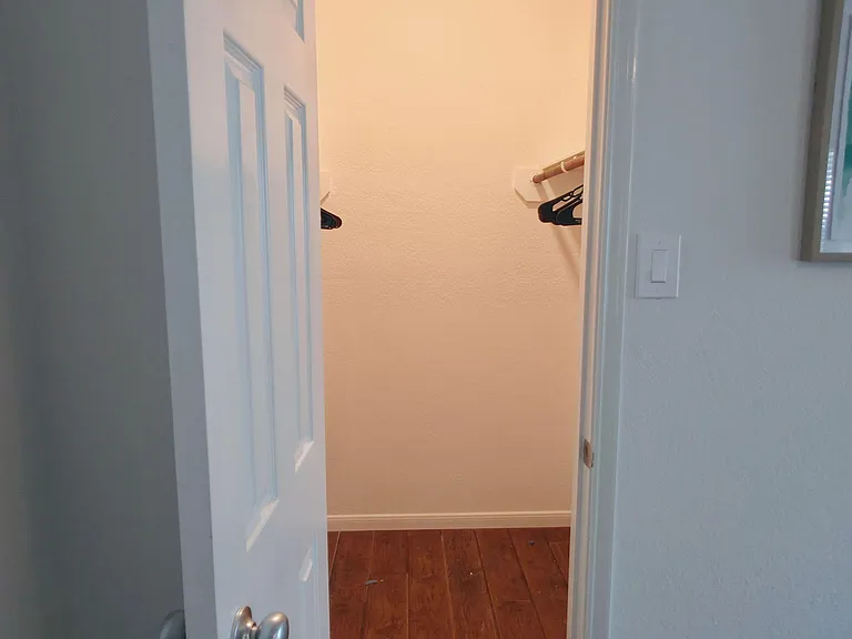 Walk-in closet space with hanging rod and shelving, plus durable wood-look flooring for easy upkeep.