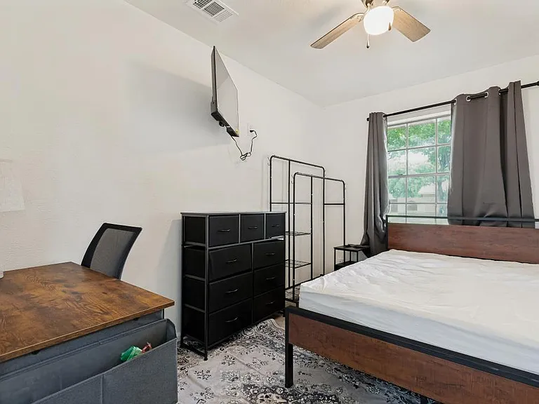 Furnished bedroom with Full Bed, Work Desk, Wardrobe and Dresser for additional storage, curtains, TV and ceiling fan.