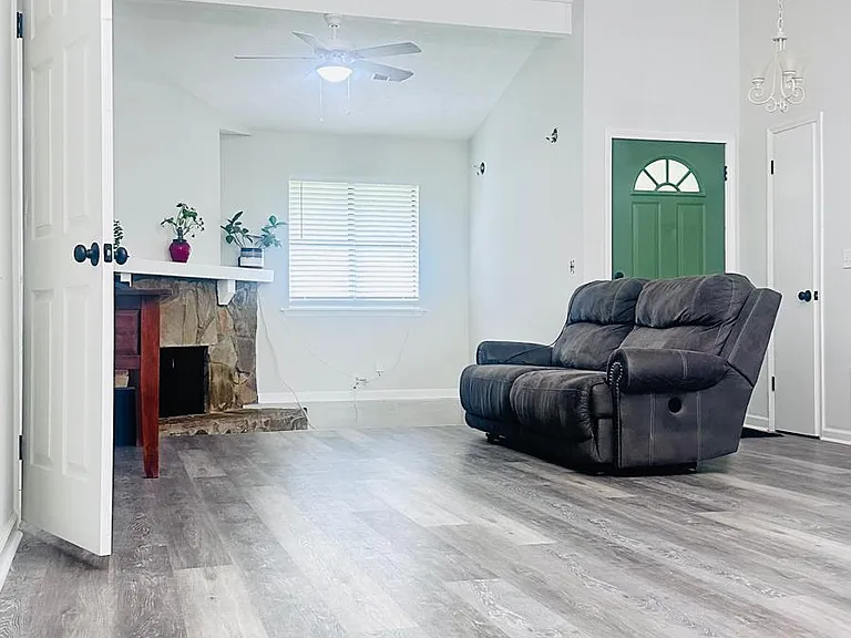 Step into a bright and inviting living space featuring soaring vaulted ceilings and a floor-to-ceiling stone fireplace that serves as the heart of the home. The spacious open-concept layout seamlessly connects the living room, dining area, and kitchen.