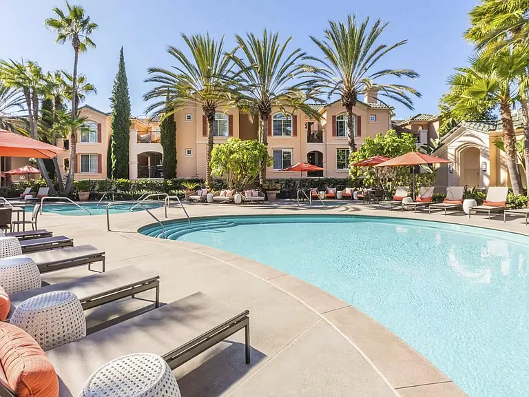 On-property resort-style outdoor pool area with lounge seating, umbrellas, palms, fire table, outdoor grilling kitchen, etc.